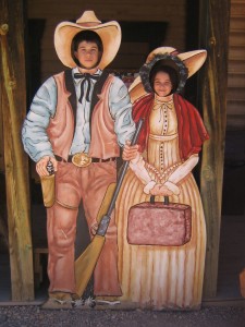 Two kids posing with their face in the cutout of two old fashioned western people