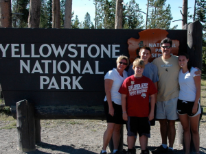 Family posing in front of the Yellowstone National Park sign in Wyoming